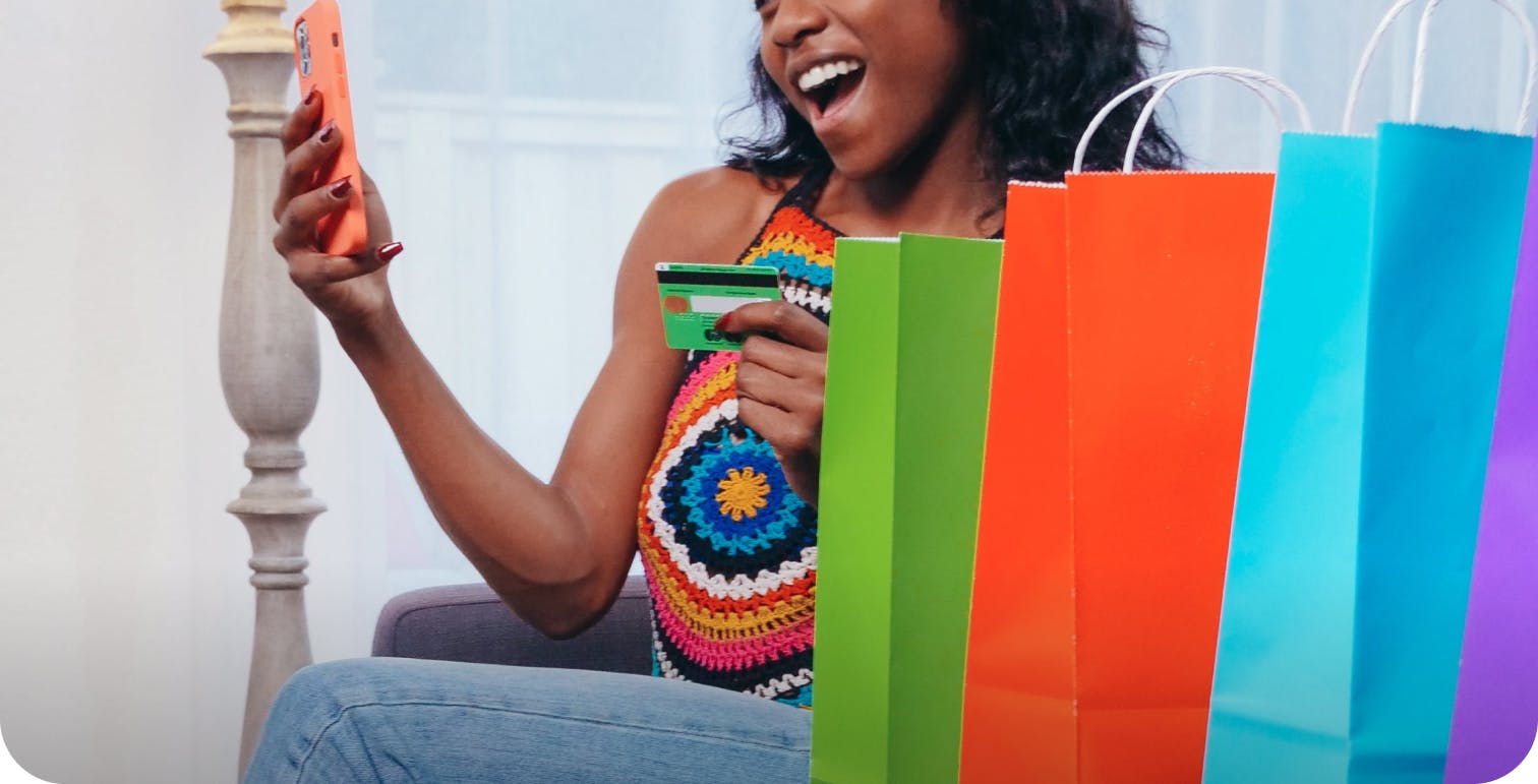 remark - woman looking at her phone and smiling with colorful shopping bags beside